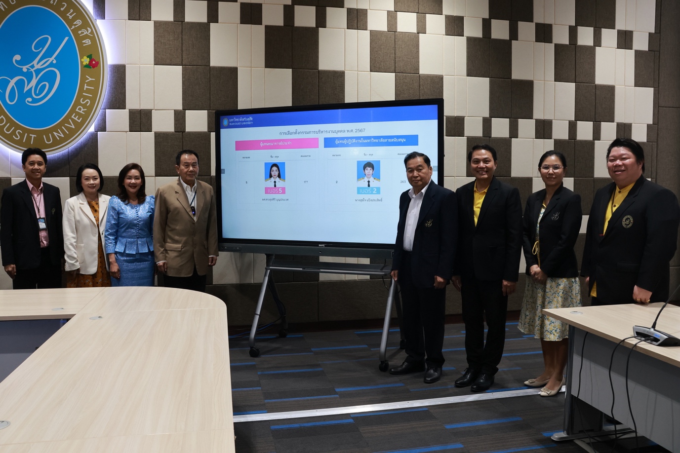 A group of people standing in front of a large screen
Description automatically generated