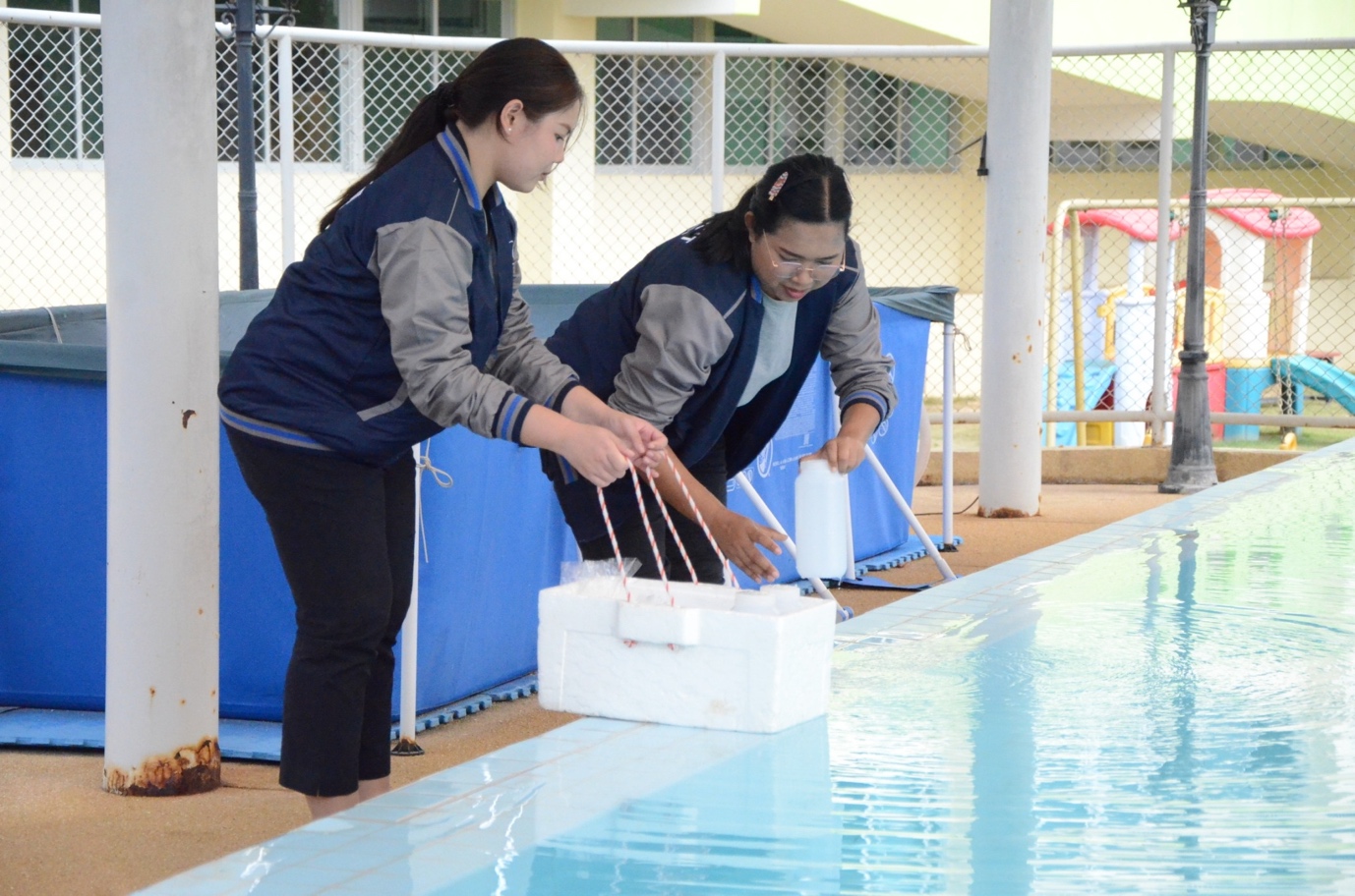Women holding a white container next to a pool

Description automatically generated
