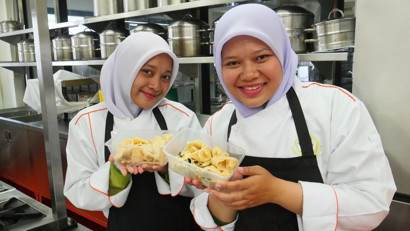 Women wearing white and black aprons holding food

Description automatically generated
